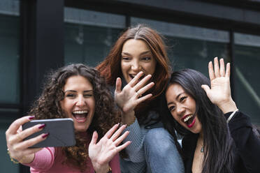 Cheerful friends waving hand to video call on mobile phone - PNAF01422