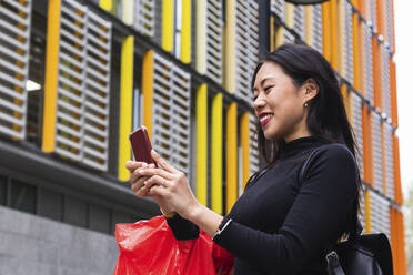 Smiling woman with backpack using mobile phone - PNAF01432