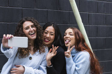 Young friends taking selfie through mobile phone by wall - PNAF01436