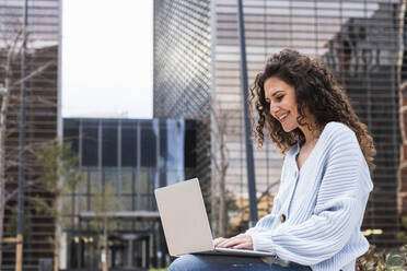 Curly hair woman using laptop in city - PNAF01447