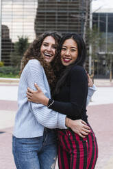 Lächelnde Freundinnen, die sich umarmen, während sie im Freien stehen - PNAF01462