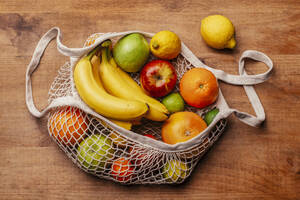 Wiederverwendbare Baumwoll-Netztasche mit frischen Früchten auf einem Holztisch liegend - RTBF01594