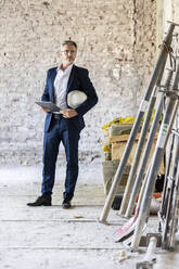 Männlicher Architekt mit Schutzhelm, der ein digitales Tablet hält, während er auf einer Baustelle steht - PESF02756