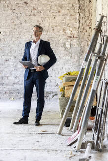 Männlicher Architekt mit digitalem Tablet, der wegschaut, während er auf einer Baustelle steht - PESF02757