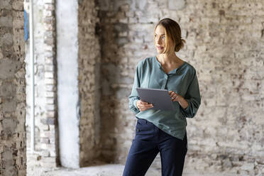 Female architect looking away while holding digital tablet at construction site - PESF02762