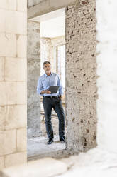 Male architect with hand in pocket holding digital tablet at construction site - PESF02779