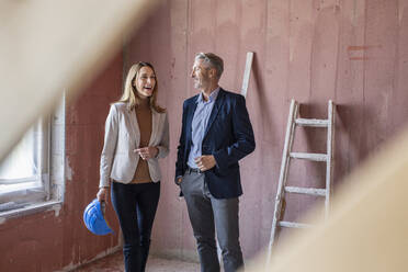 Lächelnde weibliche Kollegin im Gespräch mit einem männlichen Architekten auf der Baustelle - PESF02797