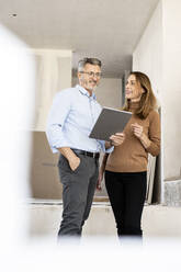 Lächelnde Kollegin, die einen männlichen Architekten betrachtet, der ein digitales Tablet auf einer Baustelle hält - PESF02799