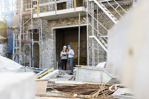 Female client discussing with male architect while standing at construction site - PESF02821