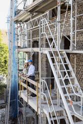 Weibliche Bauherrin zeigt einem männlichen Architekten die Konstruktion, während sie auf dem Balkon der Baustelle steht - PESF02822