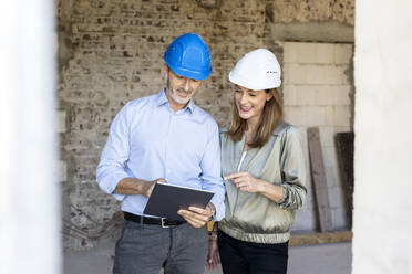 Female client and male architect wearing hardhats while discussing over digital tablet at construction site - PESF02823