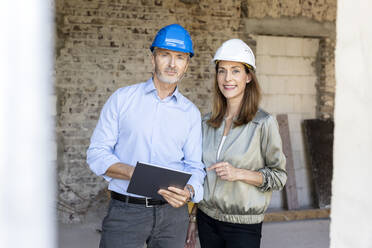 Männlicher Architekt mit digitalem Tablet neben einer Bauherrin auf einer Baustelle - PESF02824