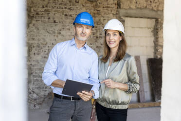 Male architect with digital tablet standing by female client at construction site - PESF02824