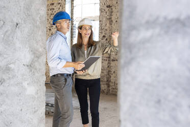 Female client gesturing while discussing with male architect at construction site - PESF02826