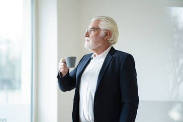 Businessman with gray hair holding coffee cup at office - MOEF03706