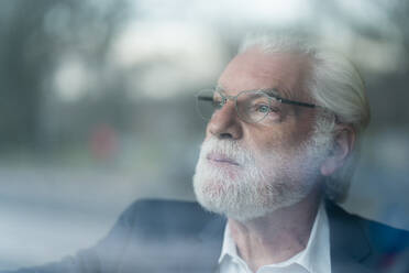 Senior businessman with gray eyes looking through window seen through glass - MOEF03709