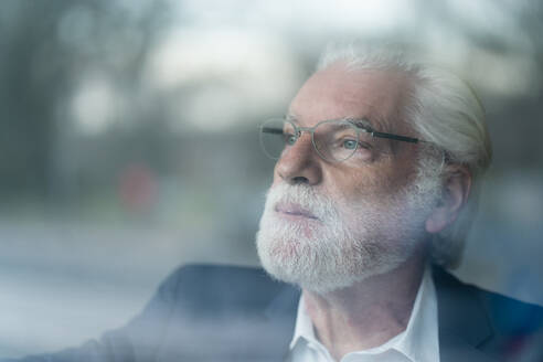 Älterer Geschäftsmann mit grauen Augen, der durch ein Fenster schaut, gesehen durch Glas - MOEF03709