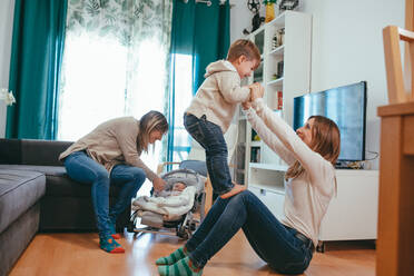 Smiling young lesbian couple playing with adorable little kids while spending free time together in modern living room - ADSF22775