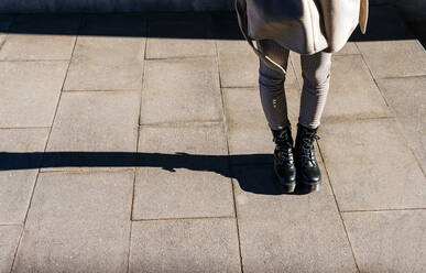 Von oben Ernte unerkennbar Frau in Stiefeln und warmen Mantel stehend auf gepflasterten Bürgersteig auf sonnigen Herbsttag - ADSF22794