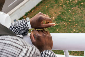 Anonymer ethnischer männlicher Unternehmer, der die Zeit auf einem modernen Armband auf einer umzäunten Brücke in der Stadt beobachtet - ADSF22810