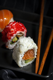 Top view Komposition von köstlichen frischen verschiedenen Sushi und Bambus-Essstäbchen auf schwarzer Platte auf karierten Tuch serviert - ADSF22830