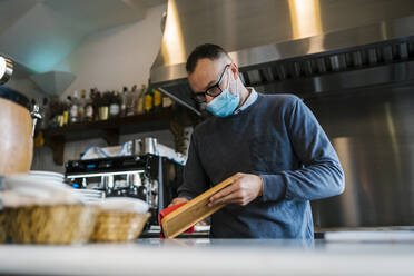 Kellner mit Gesichtsschutzmaske wischt Holztablett an einer Bar ab - EGAF02293