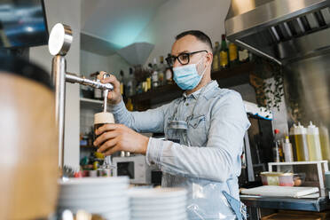 Kellner, der in einer Bar während einer Pandemie Bier in Gläser füllt - EGAF02299