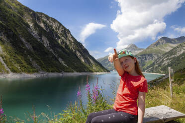 Girl pointing while sitting on bench amidst meadow at Zillergrund, Austria - GAF00178