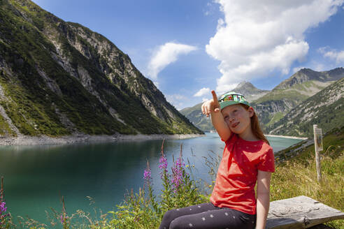 Mädchen, das auf einer Bank inmitten einer Wiese im Zillergrund, Österreich, sitzt und zeigt - GAF00178