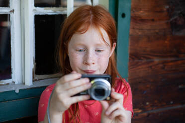 Redhead girl photographing through camera by window - GAF00185