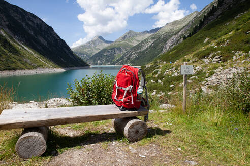 Backpack on wooden bench during sunny day at Zillertal, Austria - GAF00194