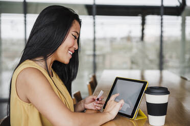 Unternehmerin beim Einkaufen mit Kreditkarte über ein digitales Tablet im Büro - EBBF03367