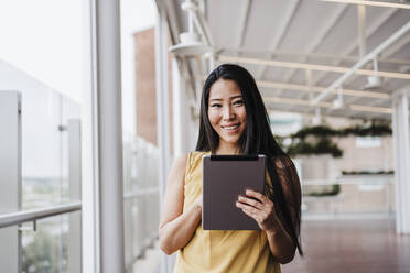 Smiling businesswoman holding digital tablet at office - EBBF03373