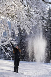 Junge Frau mit erhobenen Armen unter einem Baum auf verschneitem Land im Winter stehend - LBF03506