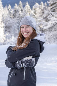 Glückliche Frau mit Strickmütze lächelt, während sie im Winter auf verschneitem Land steht - LBF03508
