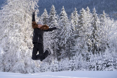 Carefree woman with eyes closed jumping on snow during winter - LBF03509