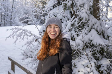 Glückliche Frau mit roten Haaren vor einem schneebedeckten Baum im Winter - LBF03512