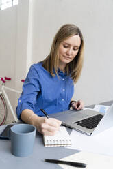 Businesswoman writing while working in office - GIOF12455