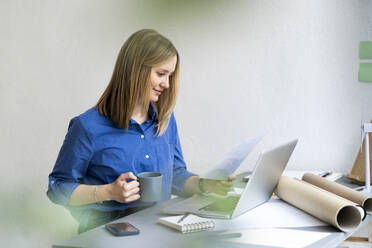 Geschäftsfrau mit Kaffeetasse, die im Büro Zeitung liest - GIOF12459