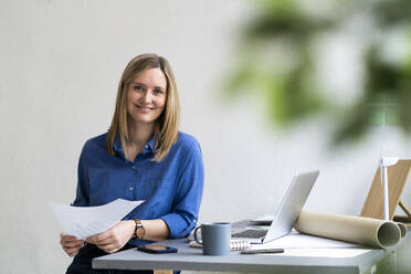 Smiling businesswoman sitting with paper in office - GIOF12460