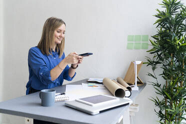 Businesswoman using mobile phone sitting at desk in office - GIOF12474