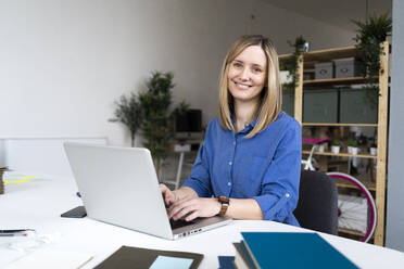 Smiling businesswoman typing on laptop at office - GIOF12480