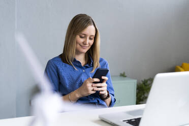 Blonde Frau, die im Büro ein Smartphone benutzt - GIOF12483