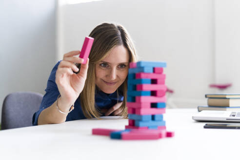 Weibliche Unternehmerin spielt Blockentfernungsspiel am Schreibtisch im Büro - GIOF12489