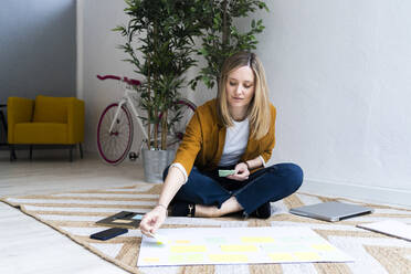 Kreative Geschäftsfrau, die auf einem Teppich sitzt und im Büro eine Strategie plant - GIOF12495