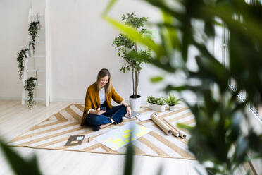 Businesswoman using mobile phone while sitting on carpet in office - GIOF12504