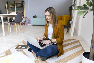 Female creative businesswoman using laptop on carpet in office - GIOF12505