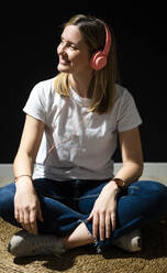 Smiling woman in headphones looking away while sitting on rug - GIOF12510