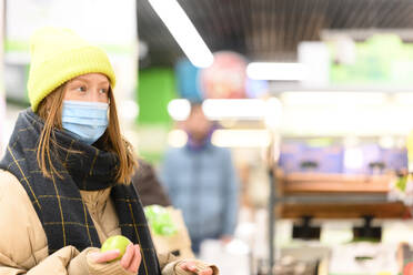 Junge Frau mit Gesichtsschutz, die beim Einkaufen im Supermarkt während COVID-19 wegschaut - VYF00589