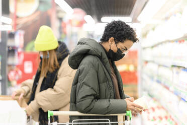 Female friends wearing protective face mask while buying groceries in supermarket during COVID-19 - VYF00595